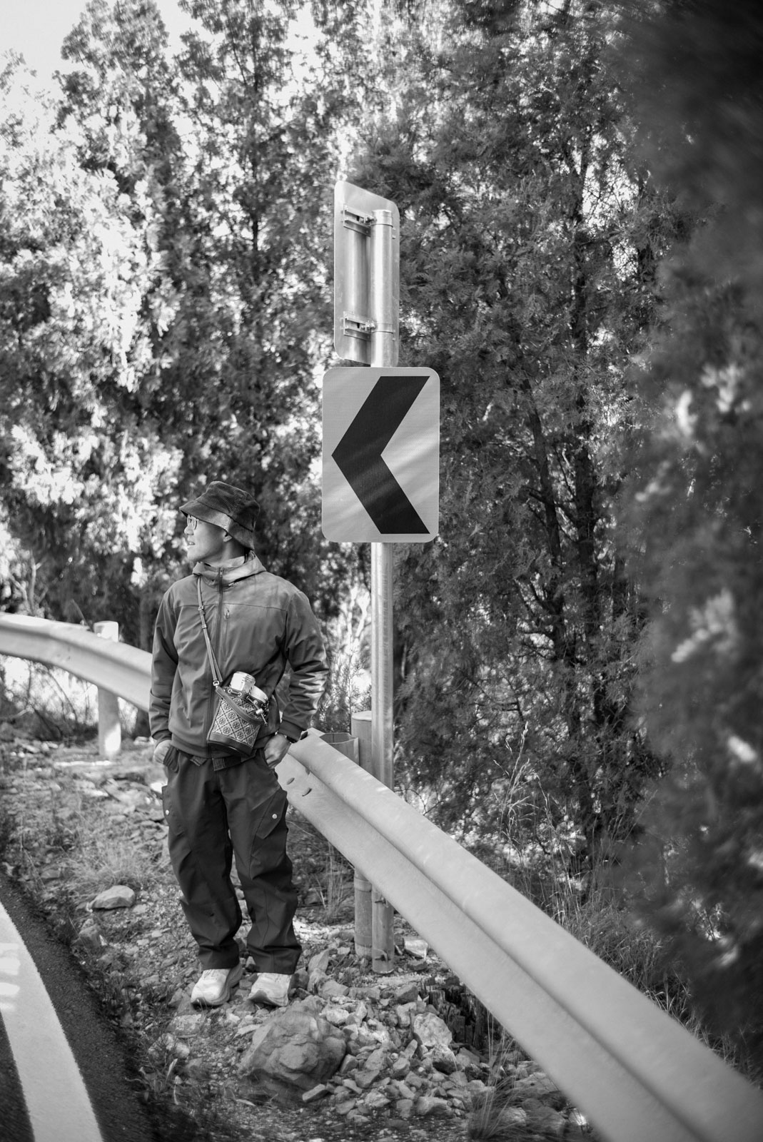 Sieh standing beside a curve sign on a wooded road